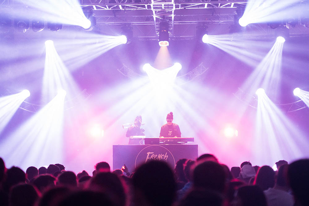 DJ facing a crowd at his deck. Photo with a purple hue